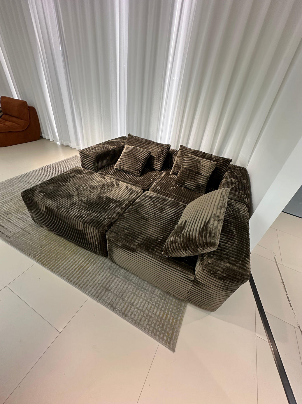 Brown corduroy sofa with cushions on a gray rug in a room with white walls and a door.