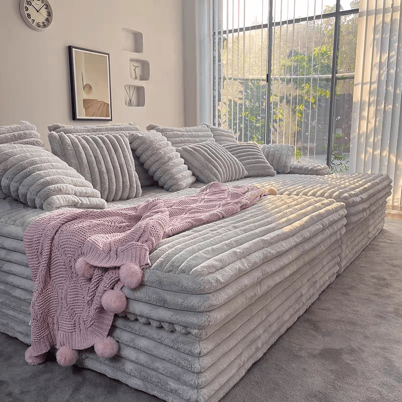 Gray plush sofa with a pink knitted blanket in a modern living room.